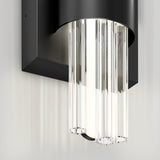 A modern wall sconce with a black rectangular base and multiple vertical, clear glass rods, creating a sleek and elegant lighting fixture against a light-colored wall.