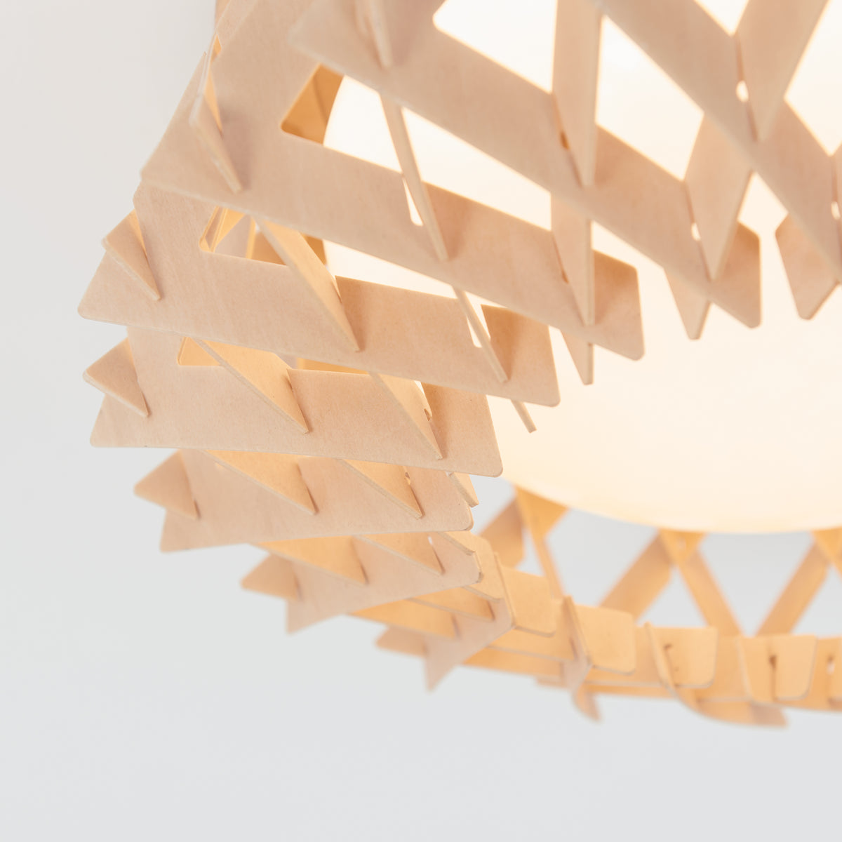 Close-up of a light fixture with a geometric, wooden lattice design around a frosted white bulb, set against a plain light background.