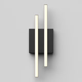 Minimalist wall light fixture with two parallel, vertical, illuminated bars mounted on a rectangular black base against a light gray background. The design is sleek and modern.