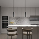 Minimalist modern kitchen with marble backsplash and countertop, two tan barstools at an island, black pendant lights, built-in ovens, a bowl of fruit, and sleek grey cabinets.