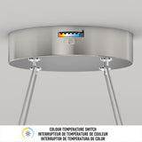 A close-up of a ceiling-mounted light fixture with a color temperature switch, labeled with a range from warm to cool tones. Metal cables suspend the fixture. Text below describes the color temperature switch in three languages.