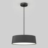 A modern black pendant light fixture with a ribbed cylindrical shade, suspended from the ceiling by a straight rod, is illuminated against a plain light gray background.