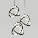 Three modern pendant lights with intertwined black and white circular rings, suspended from the ceiling against a plain light gray background. The rings emit a soft, even glow.