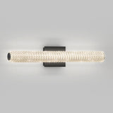 A modern wall sconce with a cylindrical, crystal-encrusted light fixture mounted on a black rectangular base, casting a soft glow on a plain light gray background.