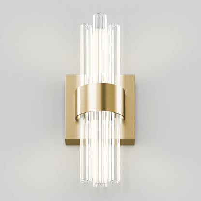The Artika Dorado LED contemporary wall sconce features vertical glass rods, a brushed gold band, and a square gold base, casting soft white light against a light gray wall.