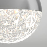 Close-up of a modern ceiling light fixture with a metallic rim and a faceted, crystal-like glass surface that reflects and diffuses light, creating a sparkling effect. The background is plain and light gray.