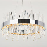 A modern, circular chandelier with a chrome frame and numerous vertical crystal prisms, illuminated by warm white lights, suspended from the ceiling on thin wires against a plain background.
