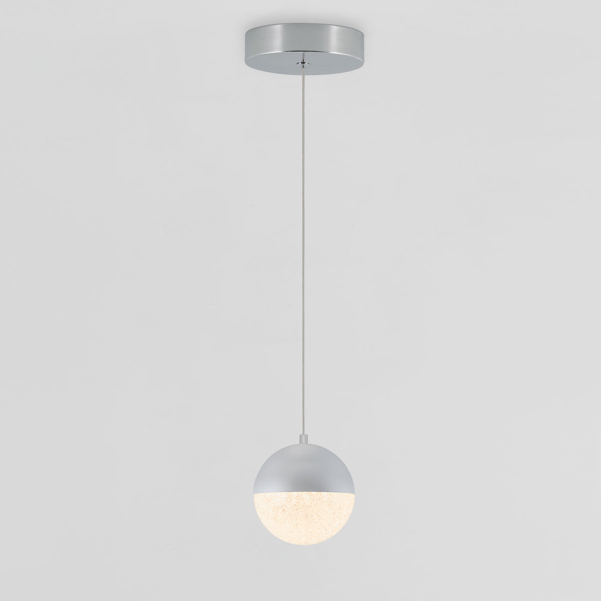A modern pendant light with a round, two-tone shade hangs from the ceiling by a thin cord. The upper half is metallic silver, and the lower half is frosted and illuminated. The background is plain white.
