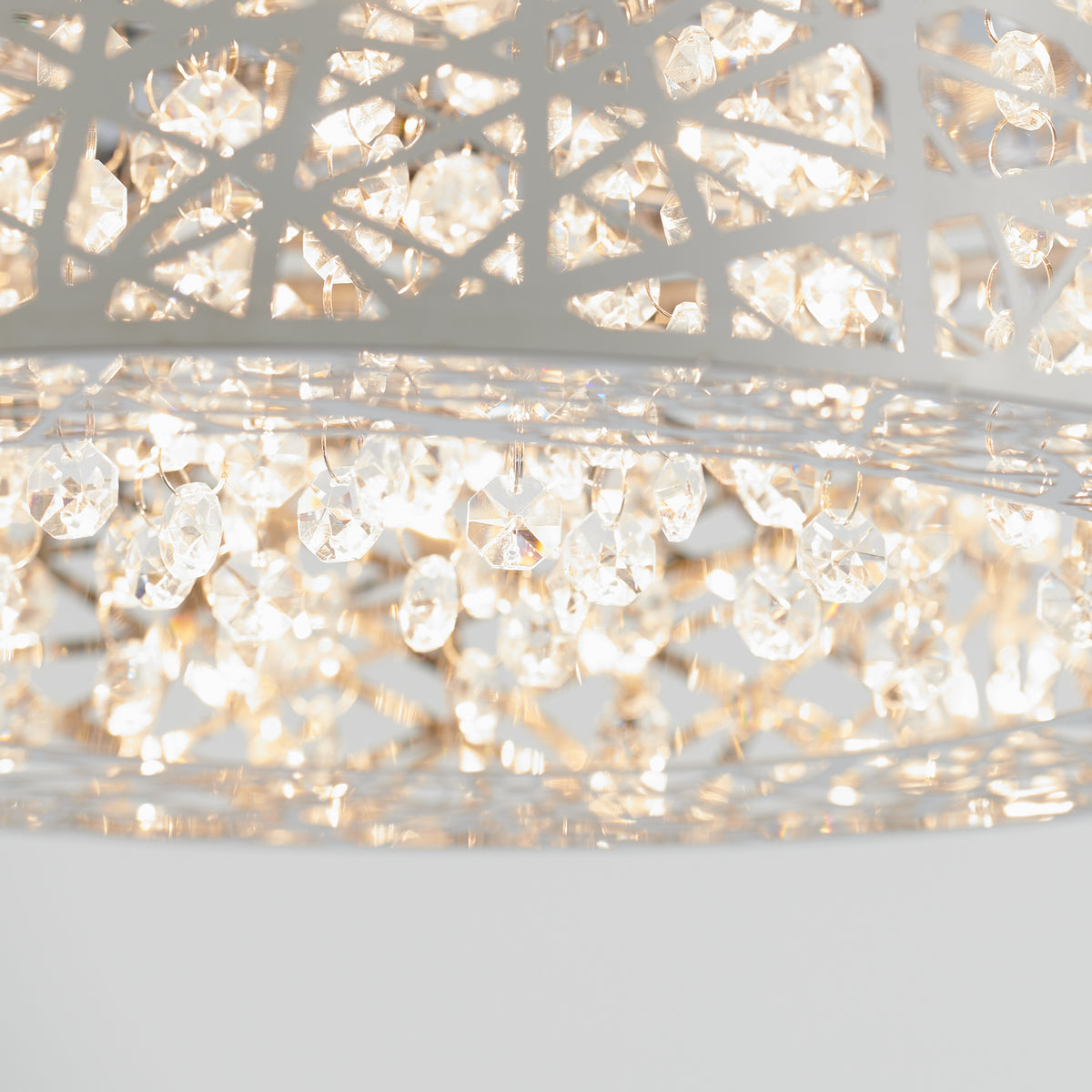 A close-up of a modern chandelier with intricate metal latticework and numerous sparkling crystal pendants illuminated by soft, warm light.