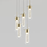 Cluster of five modern pendant lights with gold accents, cylindrical clear glass shades, and textured glass diffusers, suspended at varying heights against a plain light gray background.