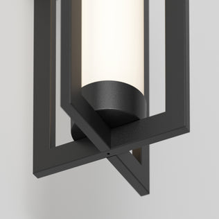 A close-up of the Artika Walt indoor-outdoor LED wall light shows its cylindrical frosted glass within a black geometric frame, mounted on a light-colored wall.