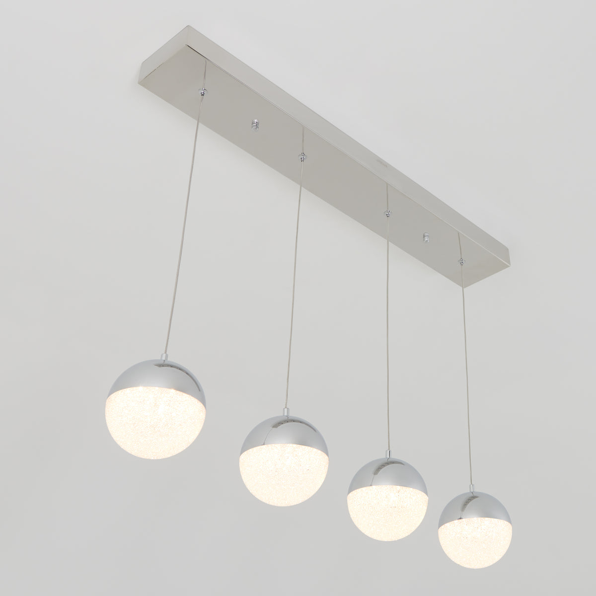 A modern ceiling light fixture with four spherical pendants, each half chrome and half frosted glass, suspended in a row from a rectangular metallic base. All four lights are illuminated.