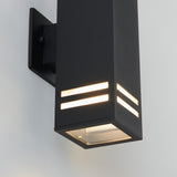 A modern black outdoor wall light fixture with a rectangular design, featuring horizontal slits emitting warm light, mounted on a light-colored wall.
