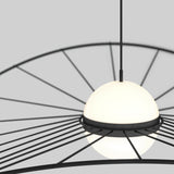 A modern pendant light with a spherical, frosted white glass shade is suspended from the ceiling. Black metal rods radiate outward in a circular pattern, creating a contemporary design against a plain gray background.