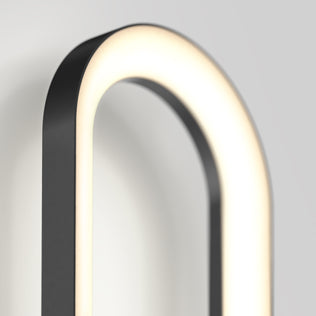 A close-up of the Artika Aiden modern LED indoor-outdoor wall light 5 CCT, featuring an oval shape and black frame, mounted on a light gray wall. The fixture emits a soft, even glow around its inner edge.