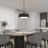 Modern dining room with a dark oval table set for six, surrounded by gray upholstered chairs. A black pendant light hangs above the table. The space features neutral decor, a vase with greenery, and a kitchen area in the background.