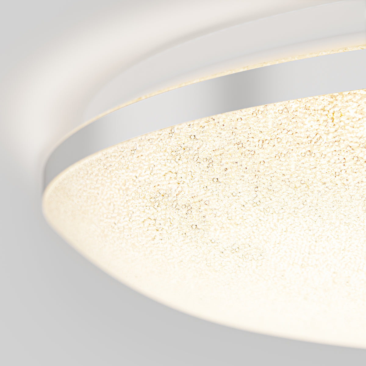 Close-up of a circular ceiling light fixture with a textured, frosted glass cover and a shiny metallic rim against a plain, light-colored background.