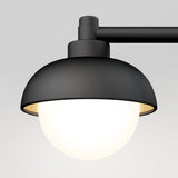 A modern black metal wall-mounted lamp with a dome-shaped shade and a glowing white lightbulb, set against a plain light gray background.