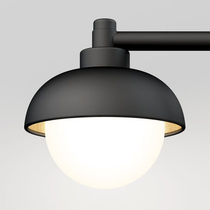 The Artika Boden LED mid-century bathroom vanity light features a modern black metal design with a dome-shaped shade and glowing white bulb, mounted on a horizontal arm against a plain light gray background.