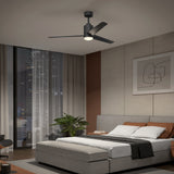 A modern bedroom with a large bed, gray upholstered headboard, blanket, and pillows, a ceiling fan with a light, abstract wall art, a plant, and a large window showing a city skyline at night.