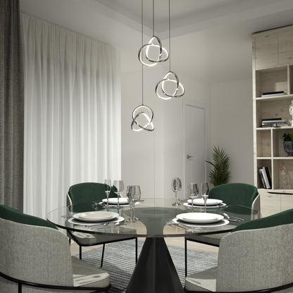 Modern dining room with a round glass table set for four, green and gray chairs, sculptural pendant lights above, white curtains, and shelves with decor in the background.