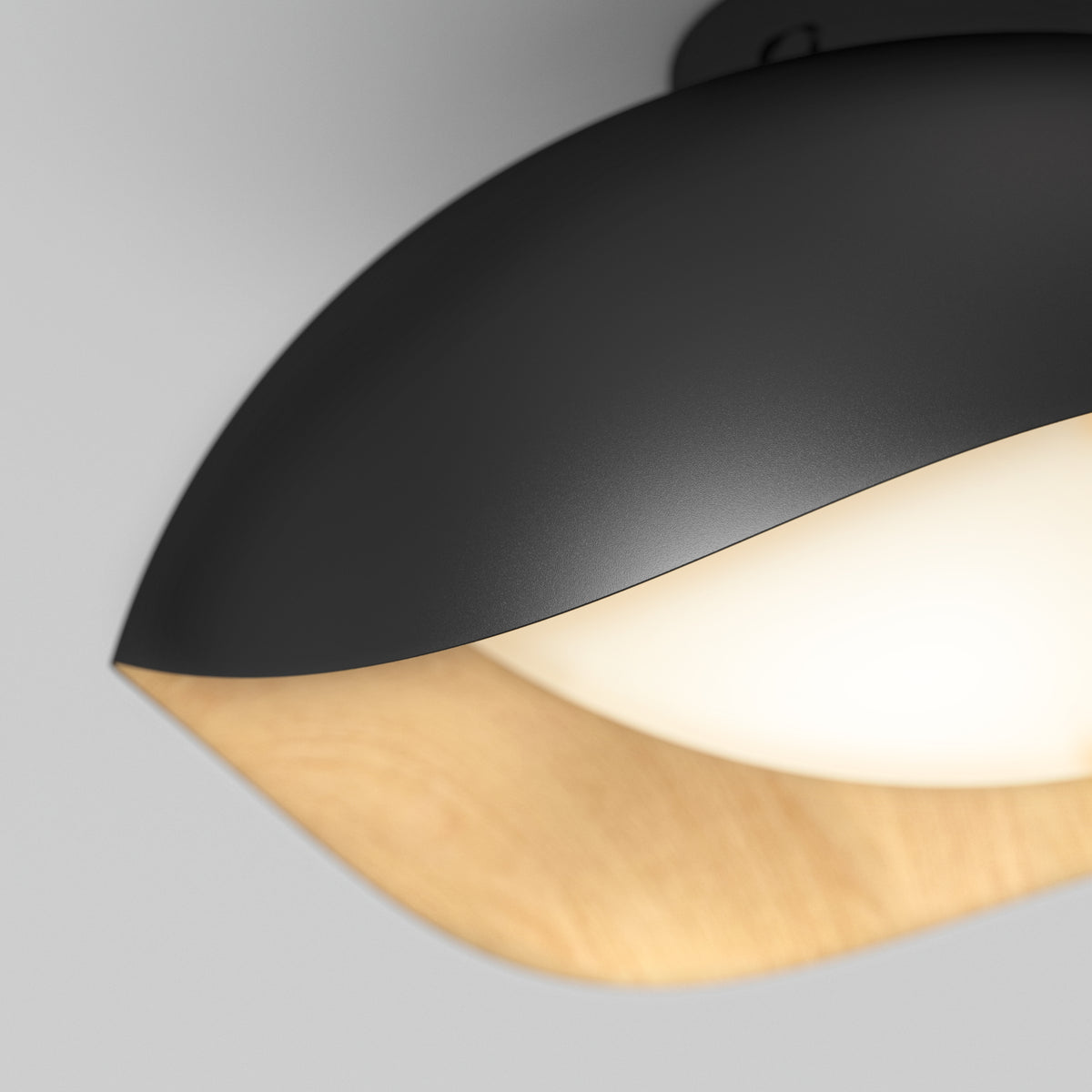 Close-up of a modern ceiling light fixture with a matte black outer shell, a smooth wooden accent, and a glowing white diffuser, set against a light gray background.
