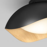 Close-up of a modern ceiling light fixture with a matte black outer shell, a smooth wooden accent, and a glowing white diffuser, set against a light gray background.