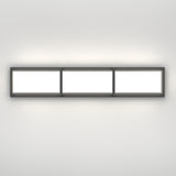 A modern rectangular wall light fixture with three illuminated panels, mounted horizontally on a plain white wall, emitting a soft glow.