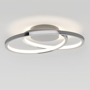 The Artika Salto LED flush mount light features two interlocking illuminated rings with a metallic base, mounted on a white ceiling. The rings provide a soft, even glow.