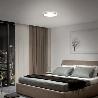Modern bedroom with a large bed, gray bedding, city view, and Artika Macy 15 in. LED RGB Wifi flush mount ceiling light.