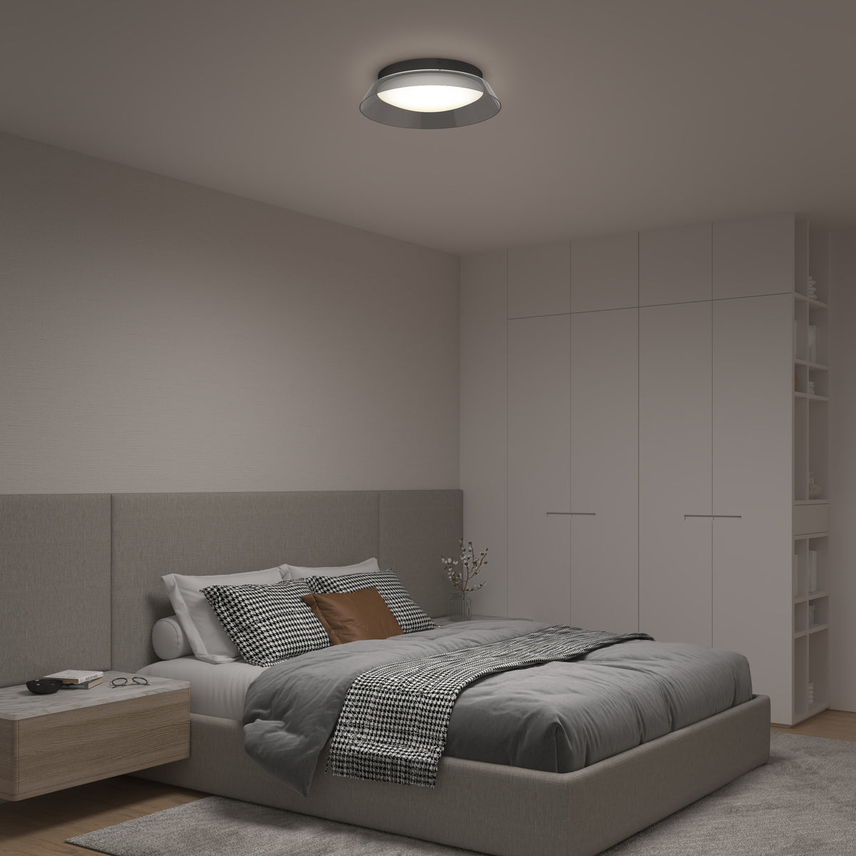 A modern bedroom with a gray upholstered bed, checkered bedding, a wooden nightstand, and built-in white wardrobes. A round ceiling light illuminates the space, which has neutral-colored walls and decor.