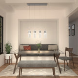 Modern dining room with a glass table, gray bench, wooden chairs, a plant, wall art, and a pendant light fixture with four lights hanging above the table. Neutral tones and minimalist decor create a cozy, inviting space.