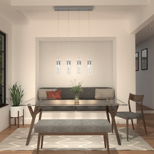 Modern dining room features a glass table, gray cushioned bench, two wooden chairs, potted plant, and Artikas Essence 4-light LED pendant hanging above. A vase of flowers sits at the center of the table.