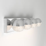 A modern wall-mounted light fixture with four spherical lamps, each half chrome and half textured glass, attached to a shiny rectangular chrome base against a white wall.