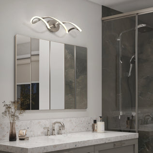 Modern bathroom with a marble countertop, sleek faucet, mirrored cabinet, decorative vase, soap dispensers, and the Artika Swirl LED bathroom vanity light above the mirror; glass shower in the background.