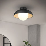 A modern, black, dome-shaped ceiling light with a bright white bulb glows in a minimalist room with gray walls and a small plant visible below.