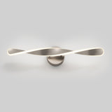 A modern wall-mounted LED light fixture with a twisted, ribbon-like design in a metallic finish, glowing softly against a plain light gray background.
