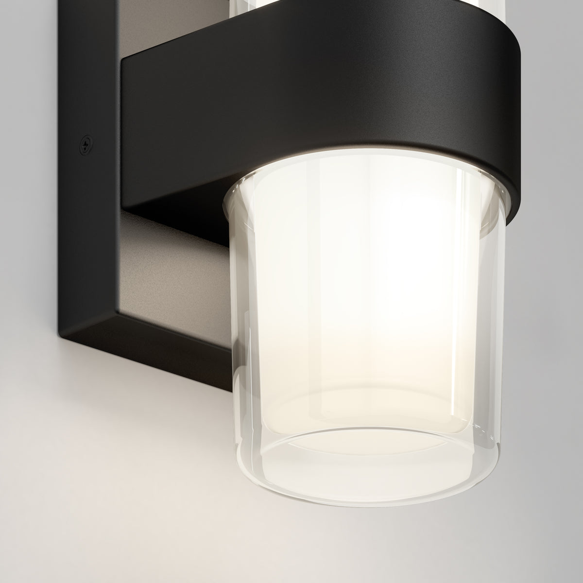 A close-up of the Artika Colton modern LED indoor-outdoor wall light 5 CCT, featuring a frosted cylindrical glass shade and black metal frame, casting a soft white glow on a light-colored wall.