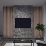 A modern living room features a flat-screen TV mounted on a gray marble accent wall, flanked by vertical wooden slats. A potted plant, glass coffee table, white rug, and light sofa complete the minimalist decor.
