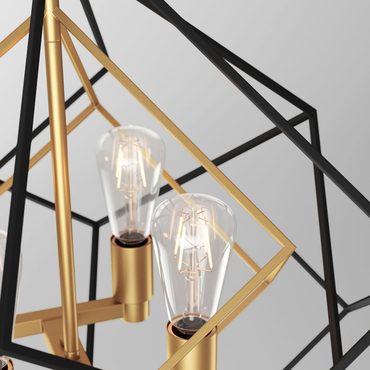 Close-up of a modern chandelier with exposed filament light bulbs in gold sockets, surrounded by intersecting black and gold geometric metal frames against a light background.