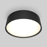 A modern, round ceiling light with a black ridged outer casing and a smooth, glowing white diffuser, mounted on a light gray ceiling.