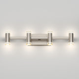 A modern brushed nickel wall sconce with four cylindrical lights arranged horizontally, each with a small round glass accent on the ends, illuminating a light gray wall.