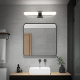 Modern bathroom with a square mirror above a rectangular sink, minimalist faucet, wooden countertop, a soap dispenser, and a small plant. A horizontal light fixture is mounted above the mirror on a concrete wall.