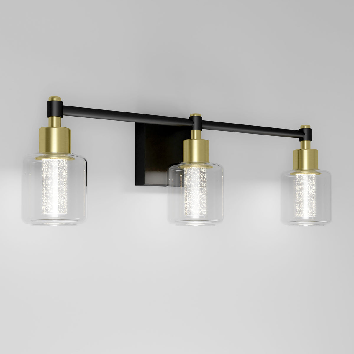 The Artika Champagne Globe bathroom vanity light features three LED lights with clear glass shades, gold accents, and a black base.