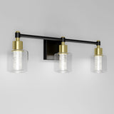 A modern wall-mounted light fixture with three cylindrical glass shades, gold accents, and a black horizontal bar on a white background.