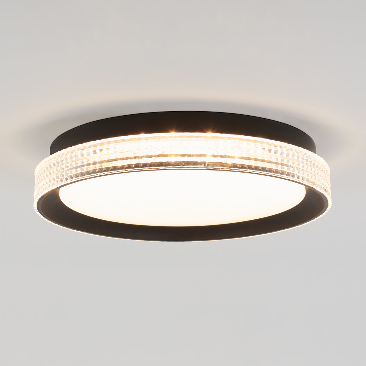 A modern ceiling light fixture with a black circular frame, a frosted white center, and a textured, illuminated outer ring against a plain white ceiling.