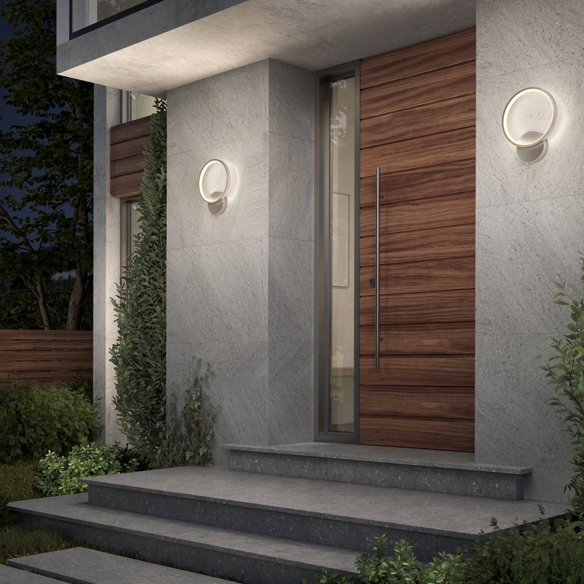 A modern gray stone entryway with a wooden door, vertical glass panel, and Artika’s Solis modern LED indoor-outdoor wall light 5 CCT brings sleek accent lighting amid greenery and concrete steps—an ideal touch for contemporary exteriors.