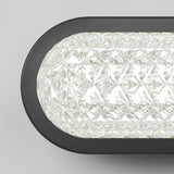 Close-up of a modern wall light fixture with a textured, diamond-patterned glass cover and a black frame, emitting bright white light against a plain gray background.