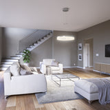 A modern living room with neutral tones, featuring two armchairs, a sofa, a coffee table, a rug, a TV on the wall, a console table, a potted plant, and a staircase with a glass railing in the background.