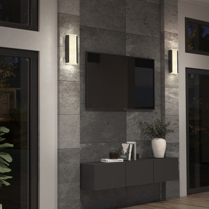 A modern living room features a mounted flat-screen TV, two Artika Blade indoor-outdoor LED wall lights, a floating black cabinet, books, decor pieces, and a white vase with greenery. A large window reflects the outdoor scenery.